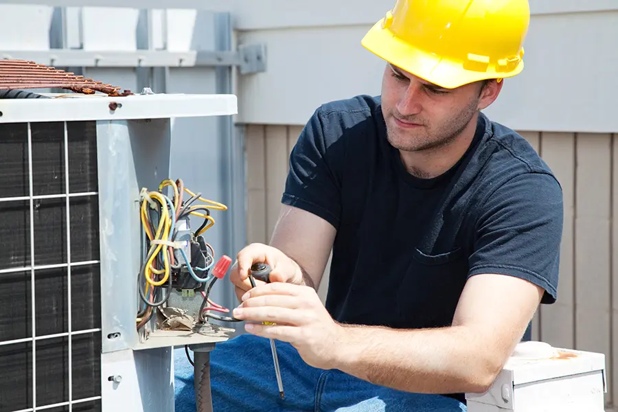 HVAC Tech in yellow hardhat examining wiring of an AC Unit