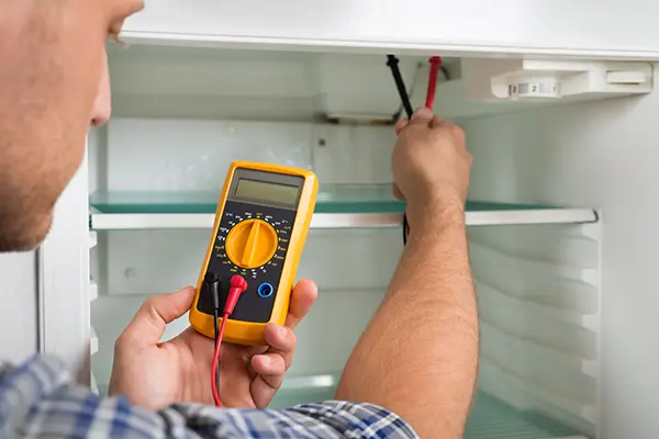 Repair technician using a multimeter to diagnose problems with a broken refrigerator