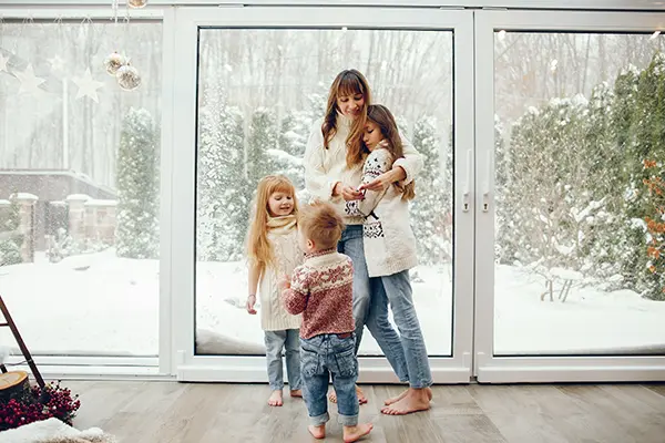 Mom and kids hugging in front of windows while it snows outside