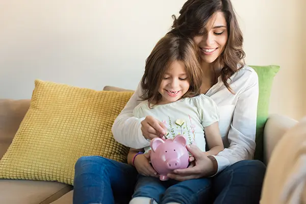 Mom and daughter sitting on a couch playing with a piggy bank